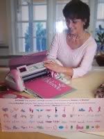 Person using a Cricut machine on a craft table with cutting mat and cartridge designs.