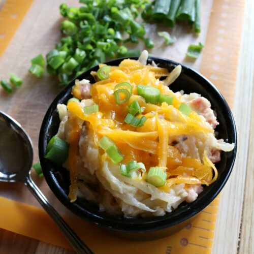 Slow cooker cheesy ham hash brown casserole topped with melted cheese and ham in a serving bowl.