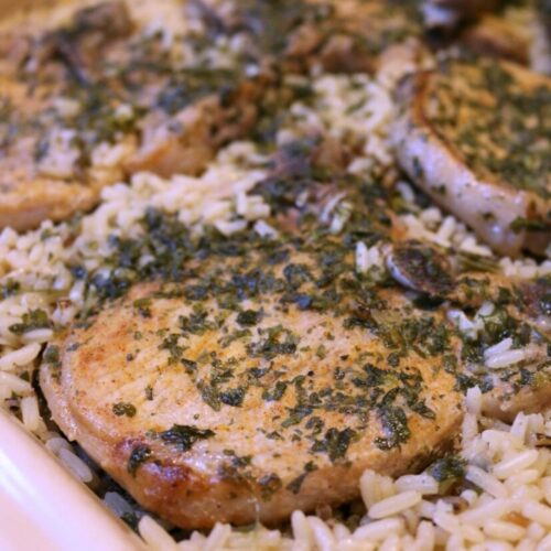 Close-up of baked pork chops served over seasoned rice in a white dish.