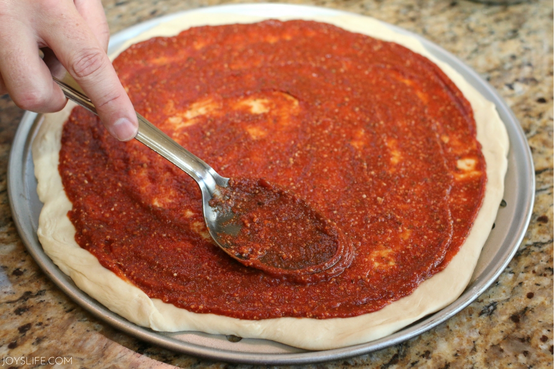 spreading pizza sauce on homemade pizza crust