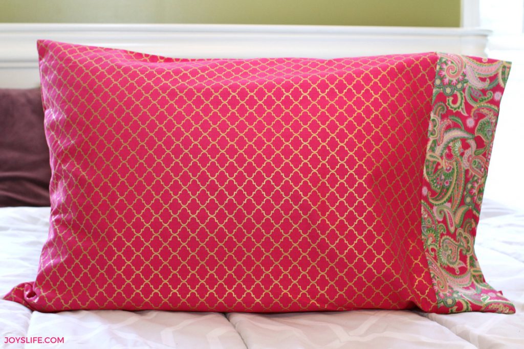 Handmade pillowcase in pink fabric with gold lattice design and paisley border, shown on a bed. Example of how fabric choices personalize pillowcases.