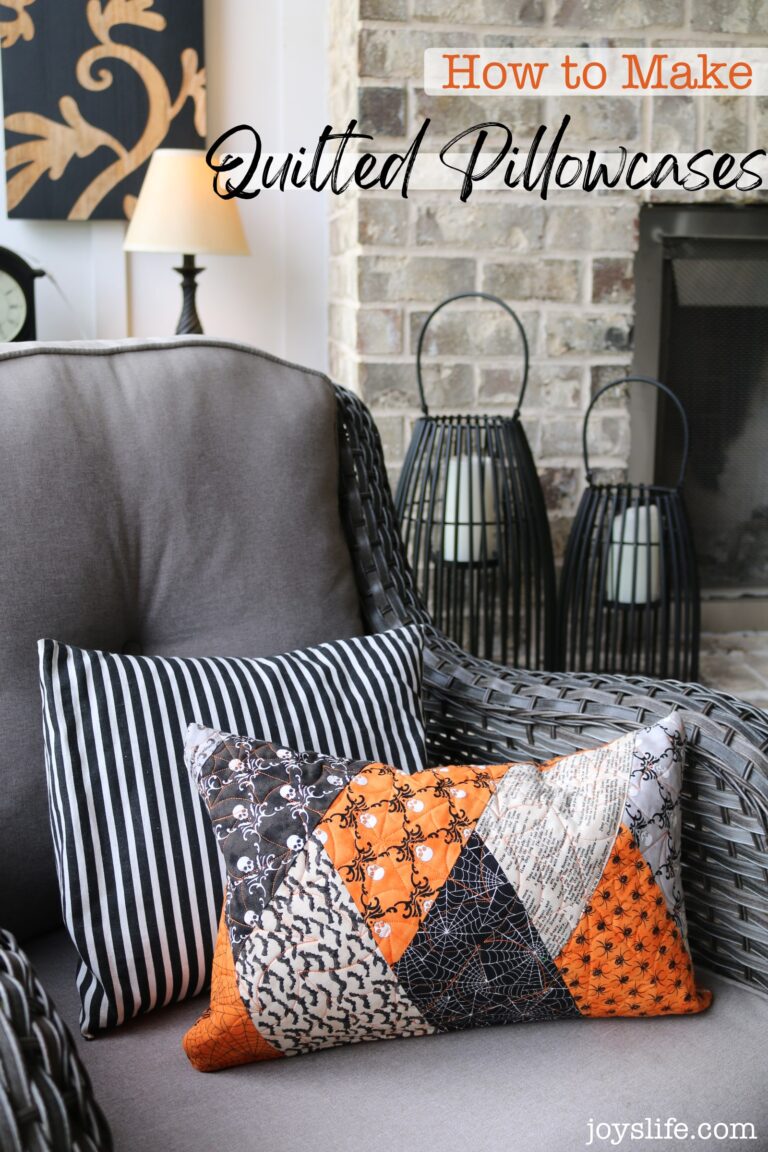 Quilted Halloween pillowcase in orange, black, and cream patchwork on a gray chair with striped pillow, styled with lanterns and a brick fireplace.