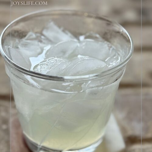 Glass of simple daiquiri cocktail on ice with text overlay that says “Simple Daiquiri Recipe JoysLife.com."