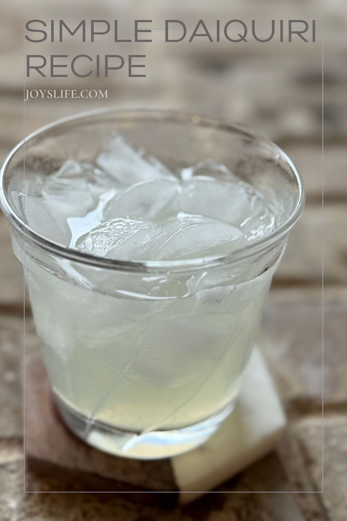 Glass of simple daiquiri cocktail on ice with text overlay that says “Simple Daiquiri Recipe JoysLife.com."
