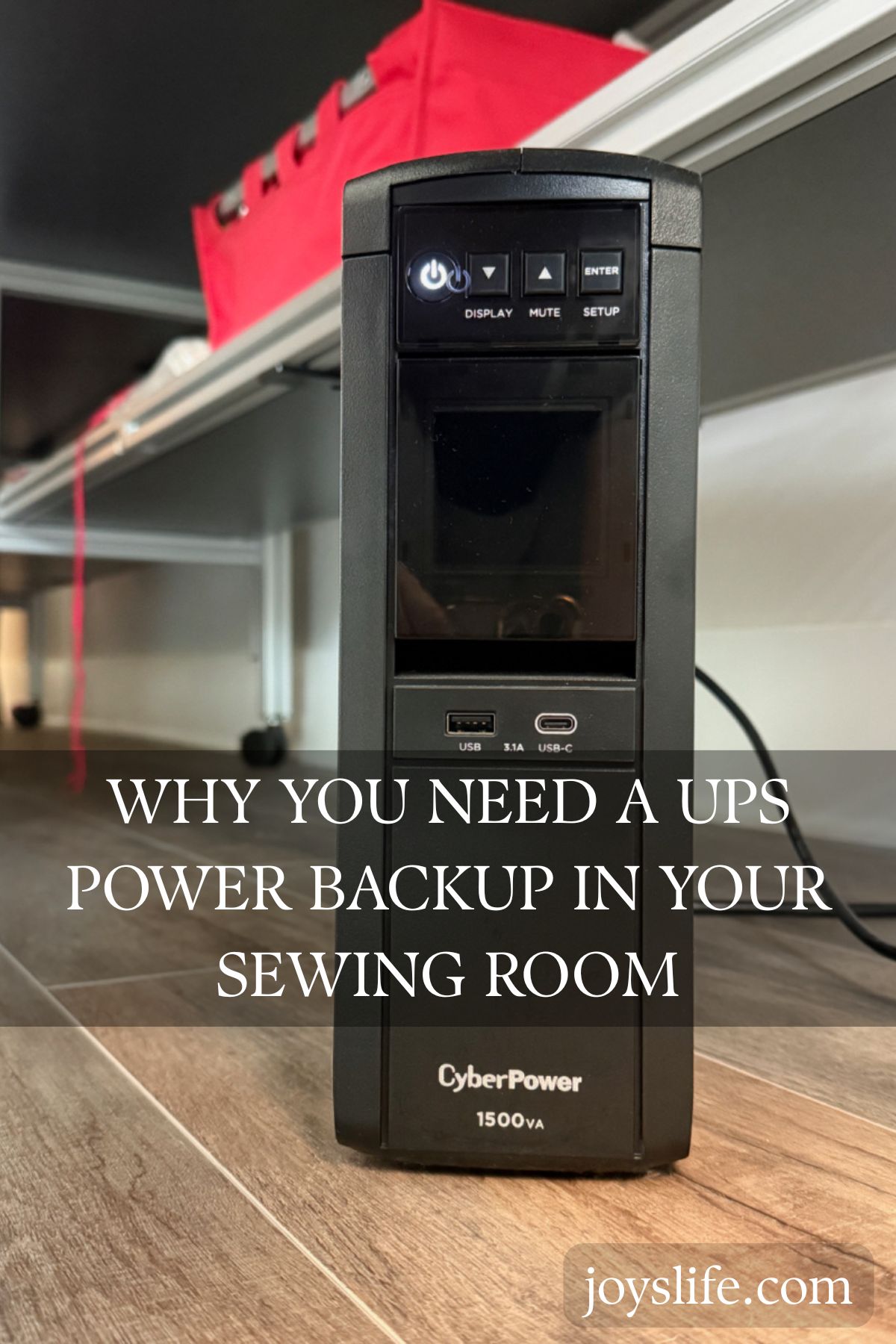 Black CyberPower 1500VA UPS power backup on wood floor in sewing room with red storage bin on shelf above.