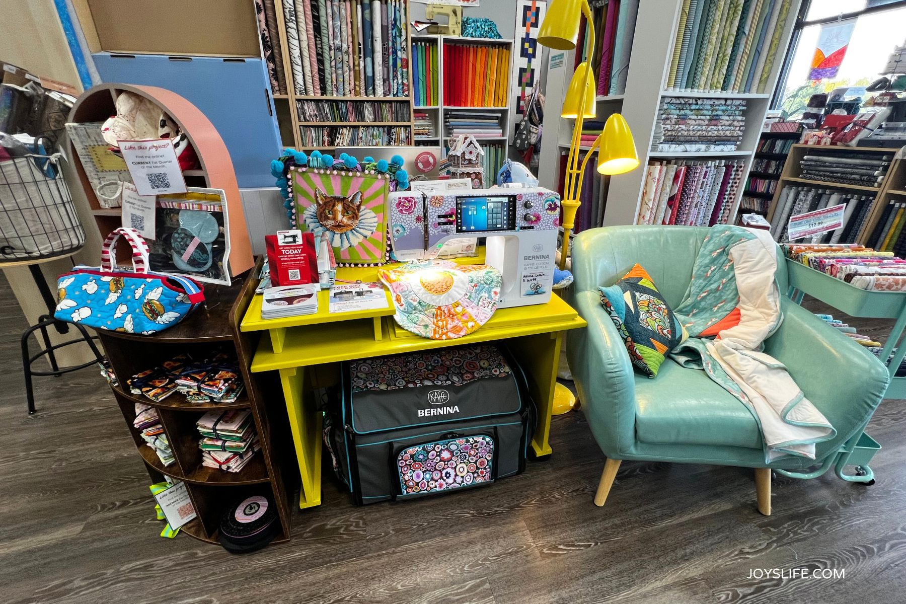 Bernina sewing machine on a yellow table with quilted projects, fabric bundles, and an aqua chair at Bernina of Naperville quilt shop.