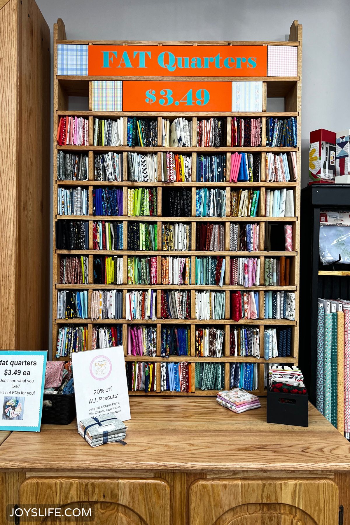 Fat quarter display wall at Quilter’s Quest in Downers Grove IL with colorful fabrics and precut bundles on a wooden counter.