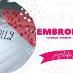 Embroidery machine stitching the word “Literally” on quilted white fabric next to red tree print fabric.