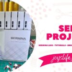 Close up of Bernina 770 QE Plus sewing quilt binding onto colorful quilt with longarm setup visible behind.