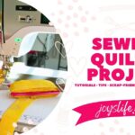 Close-up of Bernina 770 QE Plus sewing quilt binding onto colorful quilt with longarm setup visible behind.