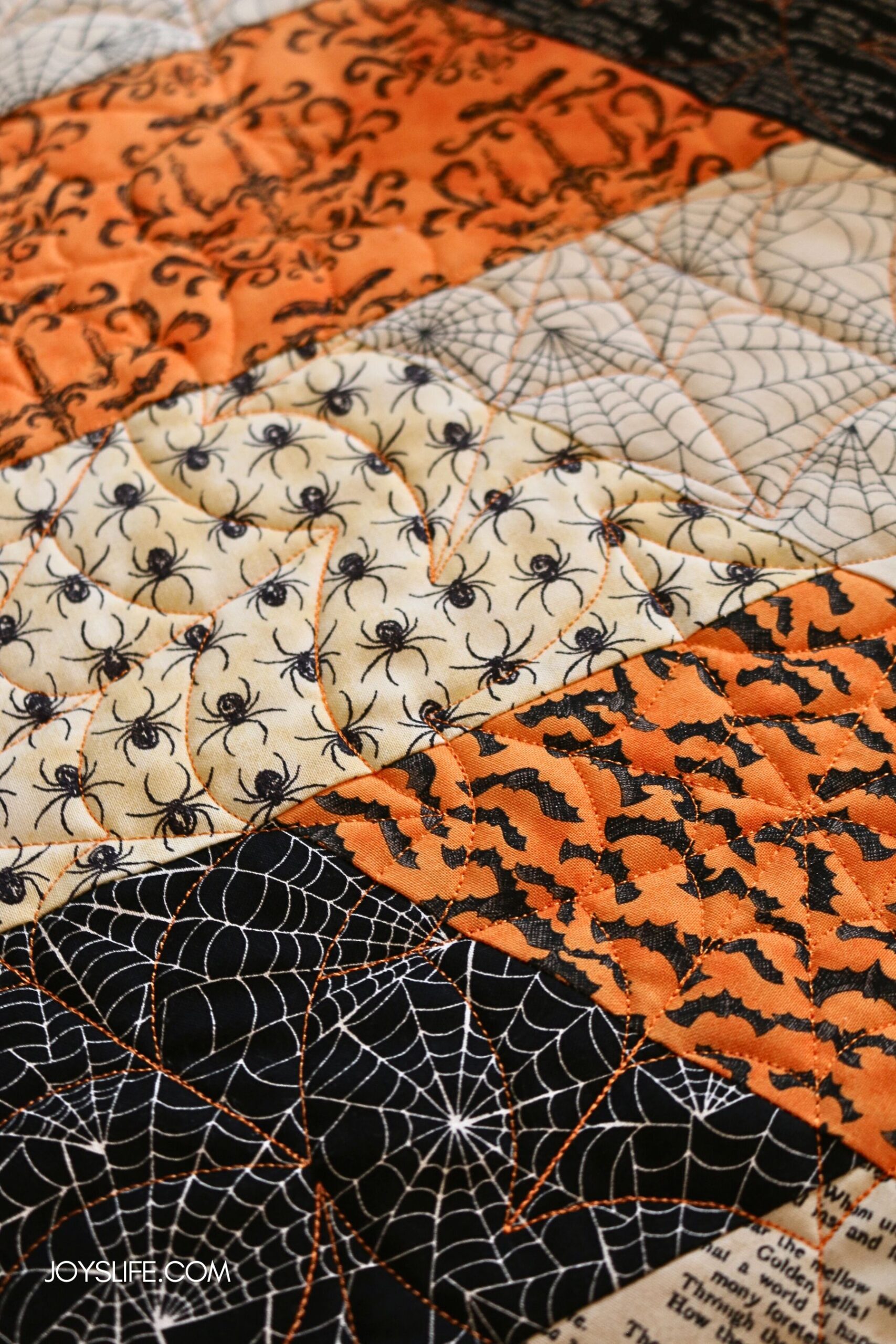 Close-up of quilted Halloween pillowcase fabric with spiders, bats, spiderwebs, and damask prints stitched together with orange quilting.