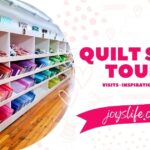 Quilt shop tours category image with colorful fabric display organized by color in white shelves, hardwood floors, and bold text overlay JoysLife.com.