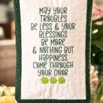 Alt Text Irish blessing mini quilt with shamrock quilting and embroidered lettering displayed on a stand. Find the tutorial at JoysLife.com.