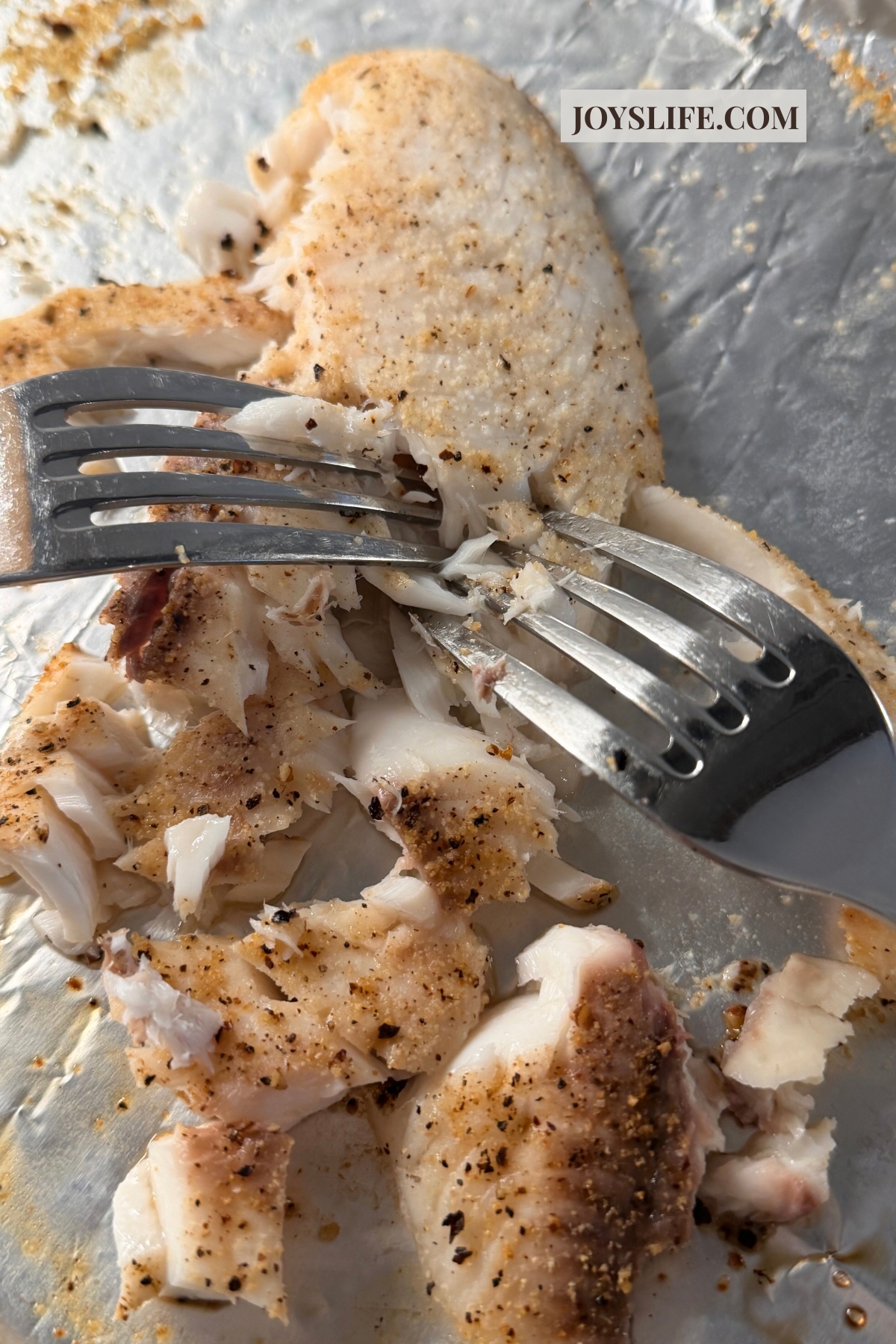 fork flaking baked tilapia into pieces for tilapia fish tacos on joyslife.com