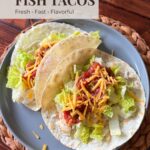 Tilapia fish tacos with lettuce, salsa, and shredded cheese on soft tortillas served on a plate.